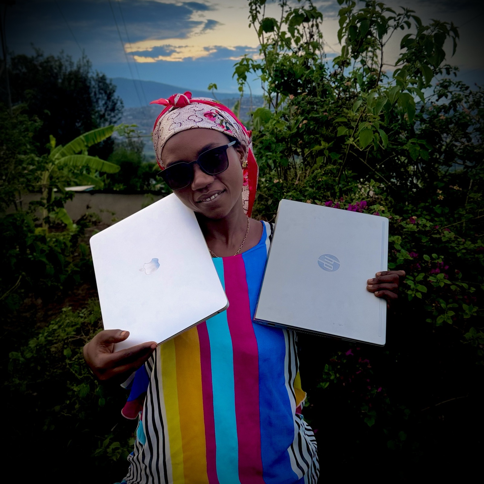 Yudita holding two laptops in a field above Kigali